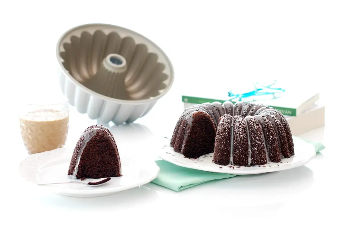 Bizcocho chocolate Thermomix, recién horneado y decorado con glaseado blanco. Un trozo ya servido con un vaso de leche.