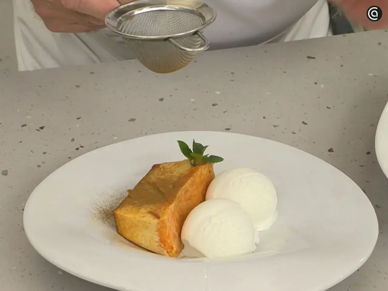 Un trozo de flan de calabaza Arguiñano, espolvoreado con canela, acompañado de dos bolas de helado de vainilla y una hoja de menta.