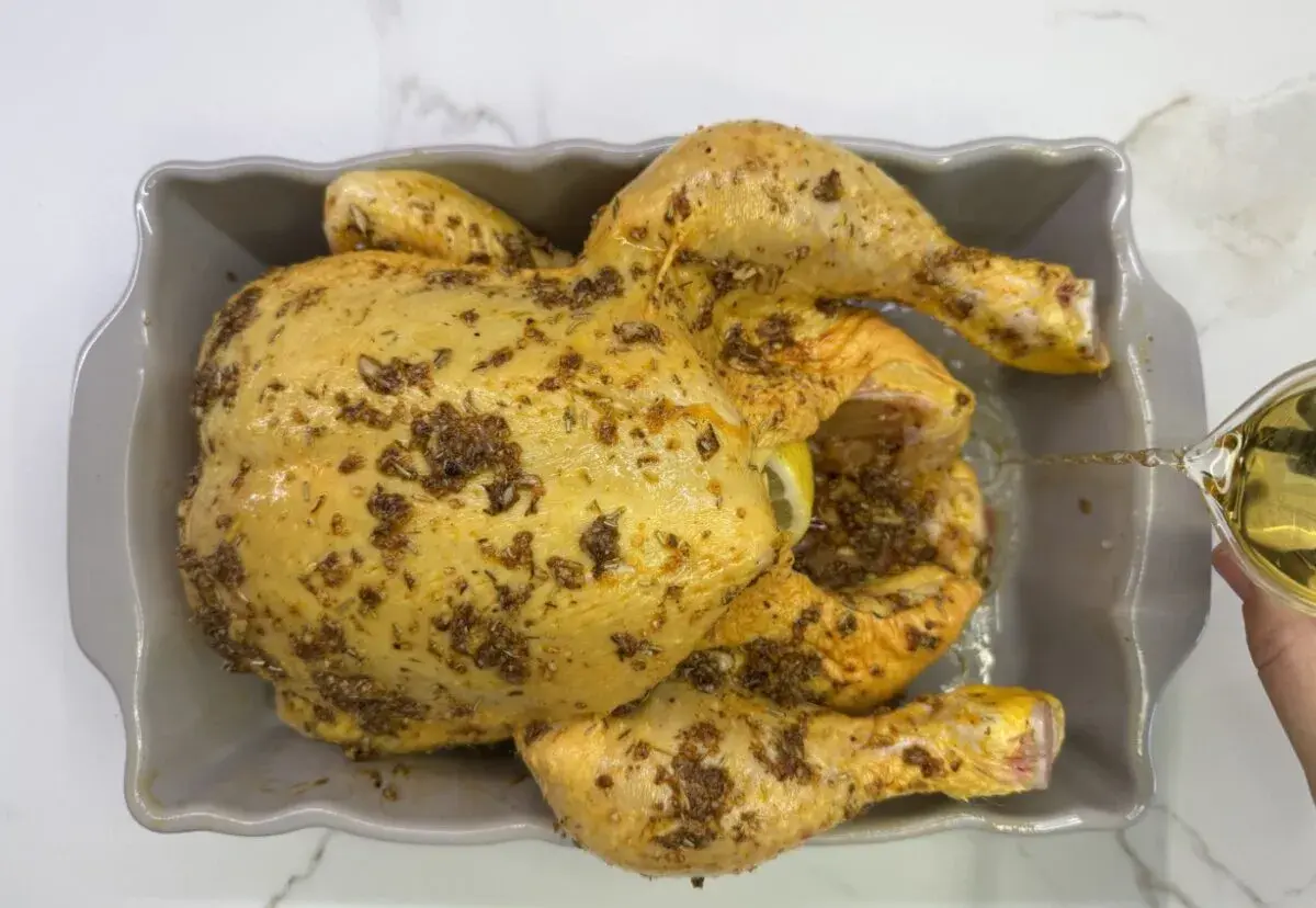 Pollo al horno crudo, sazonado y listo para asar, con un chorrito de aceite cayendo sobre él.