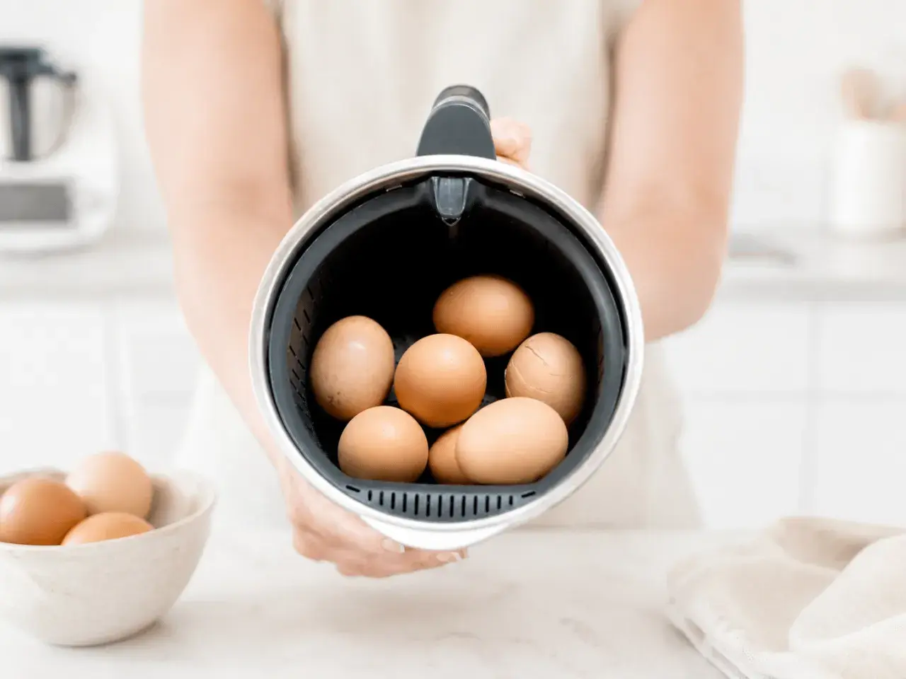 Manos sostienen el recipiente de la Thermomix lleno de huevos, listos para cocer huevos thermomix.