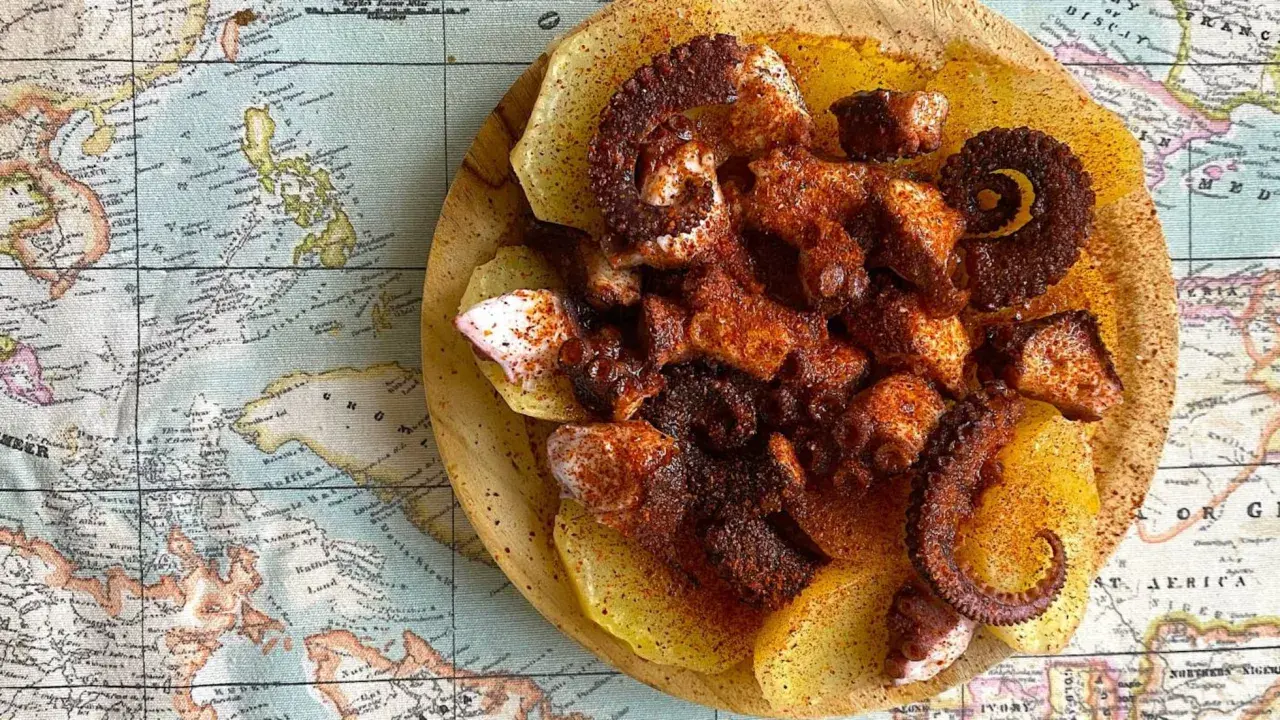 Pulpo con patatas, un plato gallego servido sobre un mapa antiguo. Tentáculos de pulpo especiados y tiernos sobre rodajas de patata.