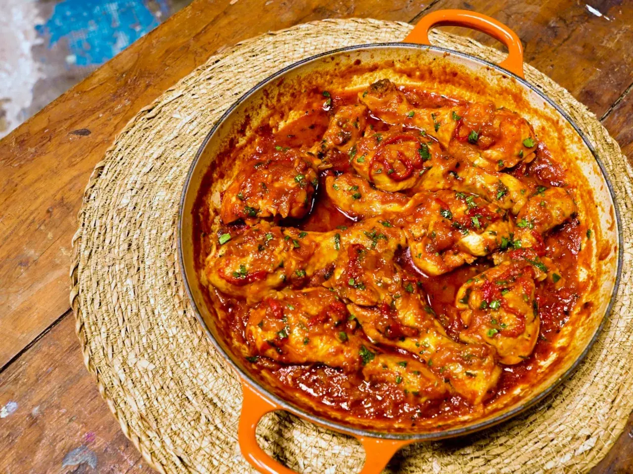 Pollo en salsa roja, como las recetas de pollo en salsa de la abuela, servido en cazuela naranja sobre esterilla de mimbre.