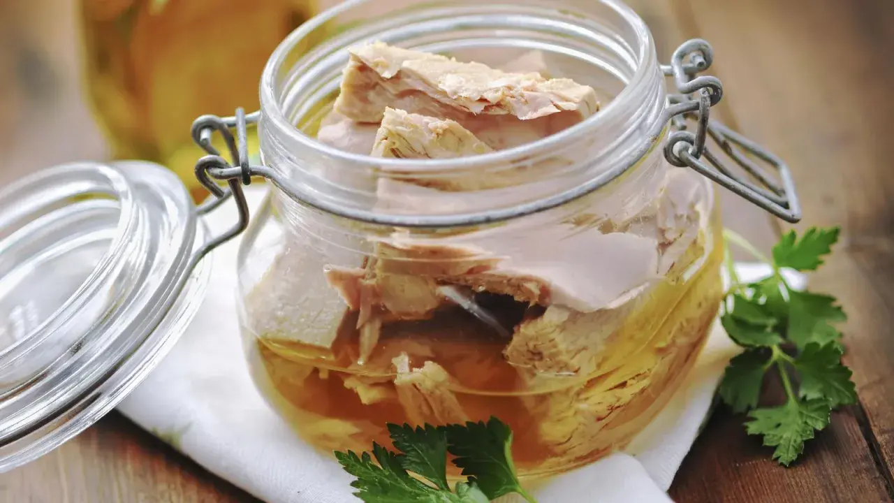 Un frasco de vidrio con atún en escabeche, listo para disfrutar. Unas hojas de perejil adornan la escena.