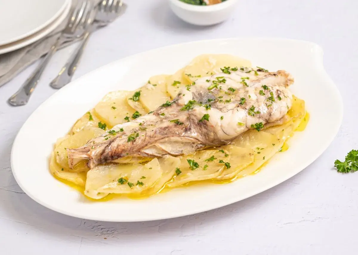 Rape al horno servido sobre patatas laminadas y espolvoreado con perejil fresco. Un plato sencillo y delicioso.