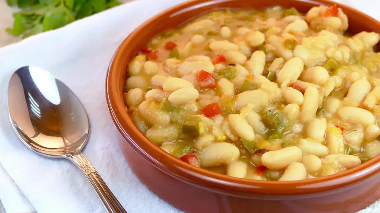 Judías blancas de bote salteadas con pimientos y cebolla, servidas en cuenco de barro.