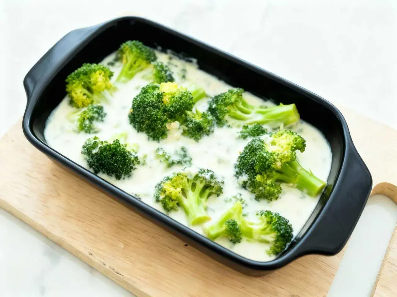 Brocoli con bechamel cremoso en una bandeja negra, listo para hornear. Un plato reconfortante y delicioso.
