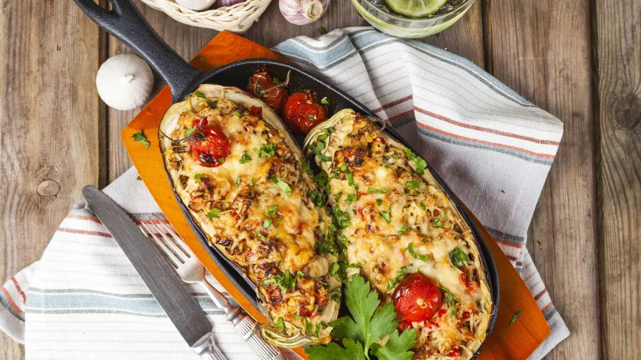 Berenjenas rellenas Arguiñano gratinadas, con tomates cherry y perejil fresco, servidas en sartén de hierro fundido.