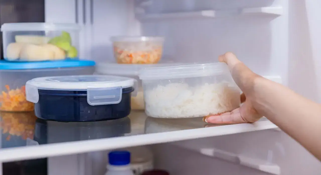 Mano saca un recipiente con arroz blanco de la nevera. Averig&uuml;emos cuanto dura el arroz en la nevera.