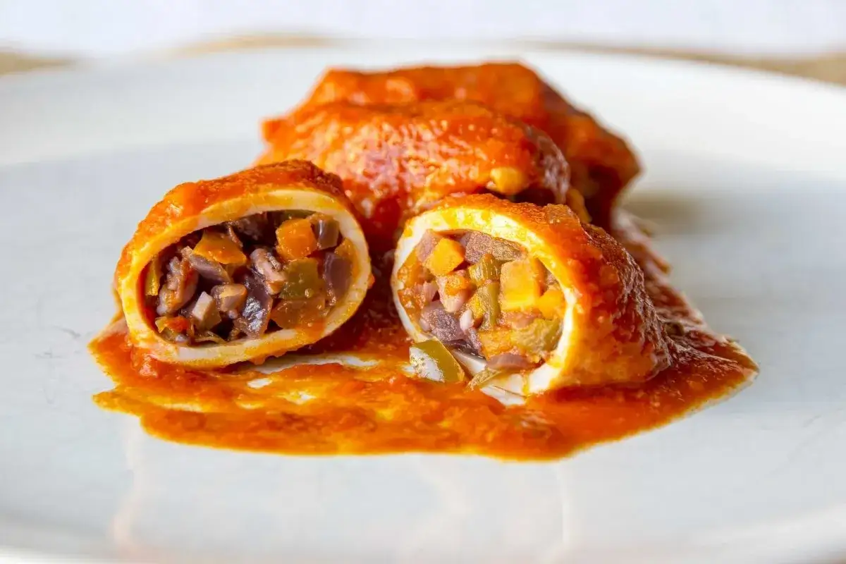 Calamares rellenos en salsa, con un corte que revela el relleno de verduras y trozos de calamar.
