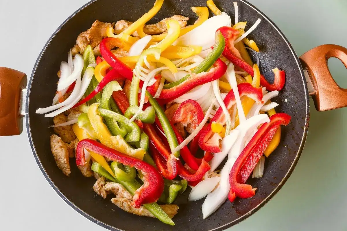 Fajitas de pollo en sart&eacute;n con pimientos de colores y cebolla, listas para cocinar.