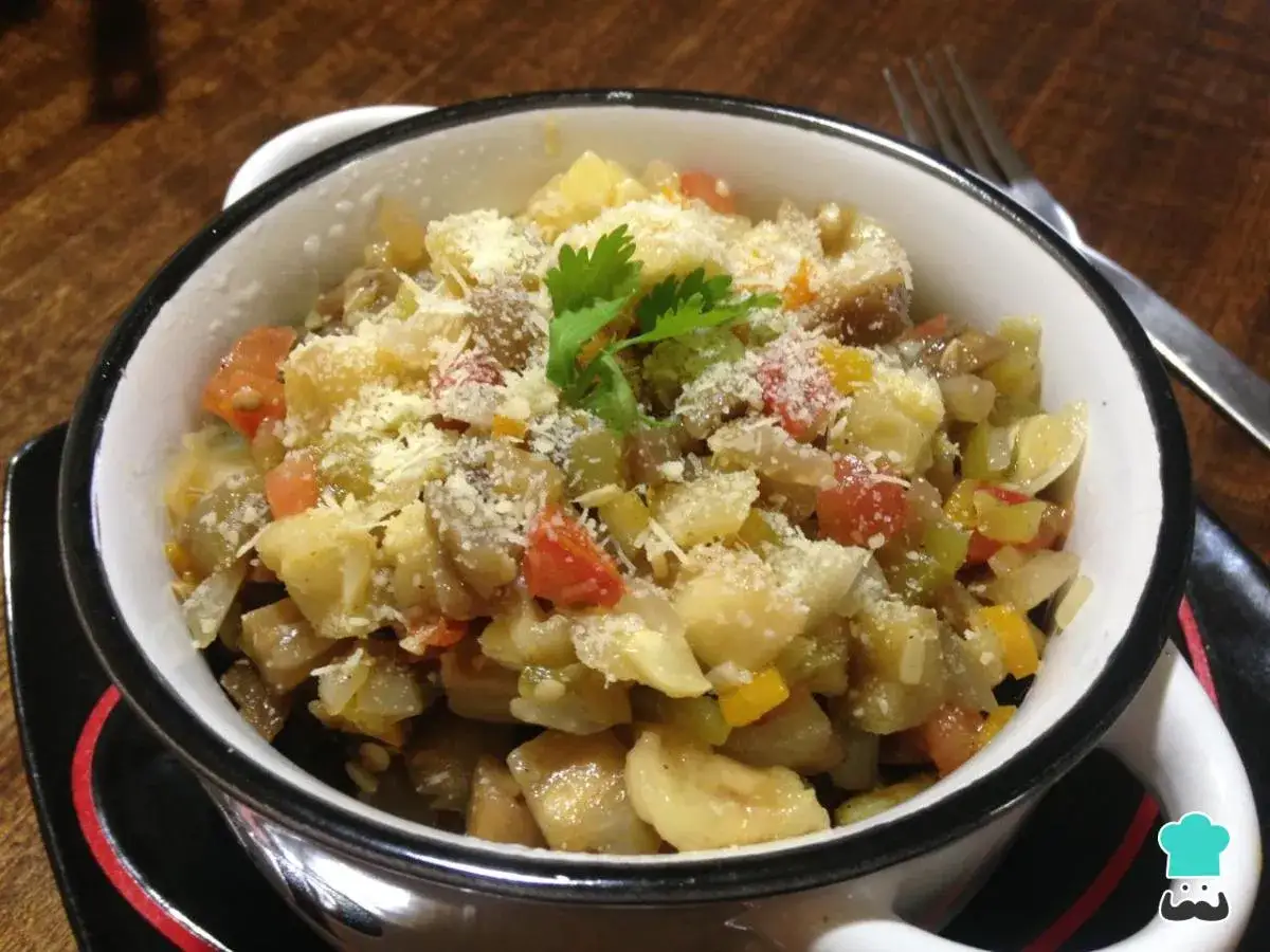 Pisto con berenjena, un plato casero lleno de verduras picadas y cubierto con queso rallado.