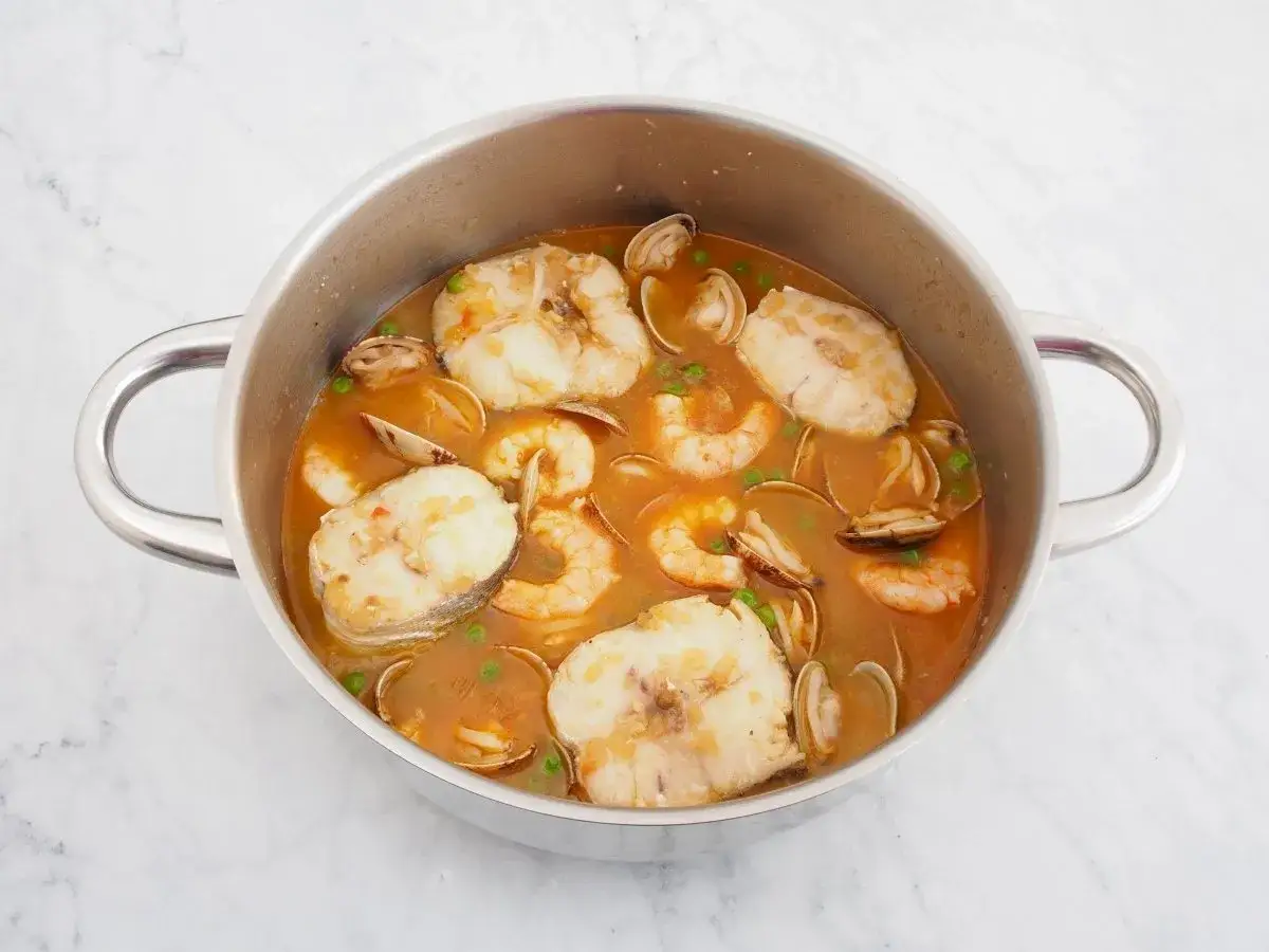 Olla con merluza en trozos, gambas, almejas y guisantes en una sabrosa salsa.