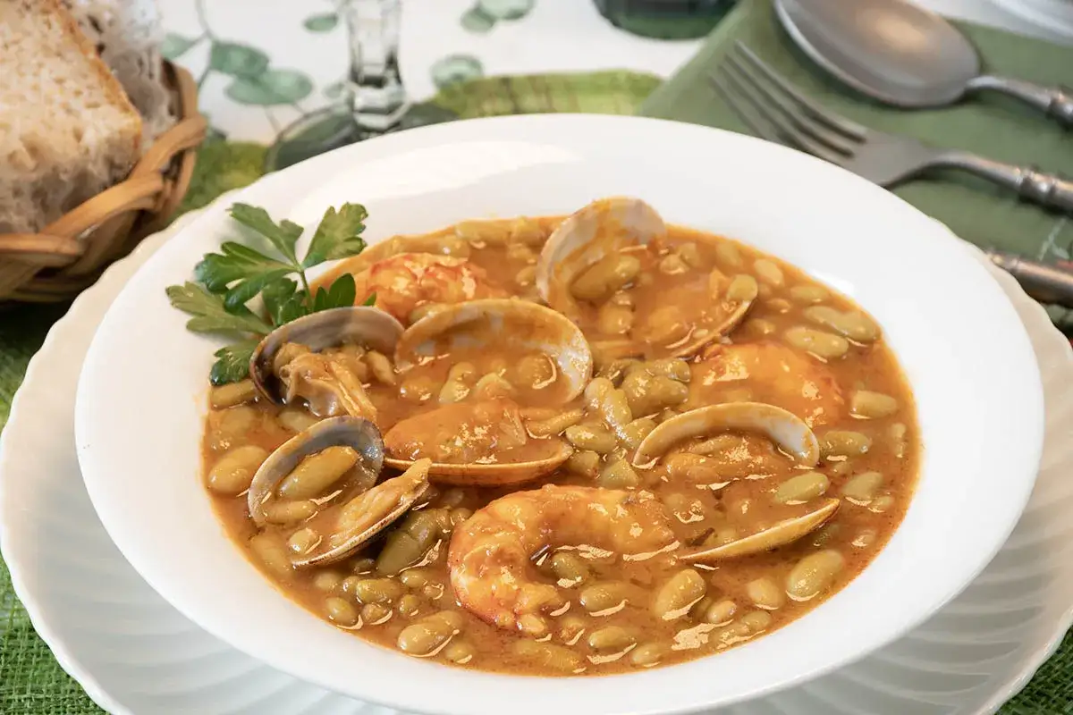 Plato de verdinas con almejas y gambas, decorado con perejil. Acompa&ntilde;ado de pan en cesta.