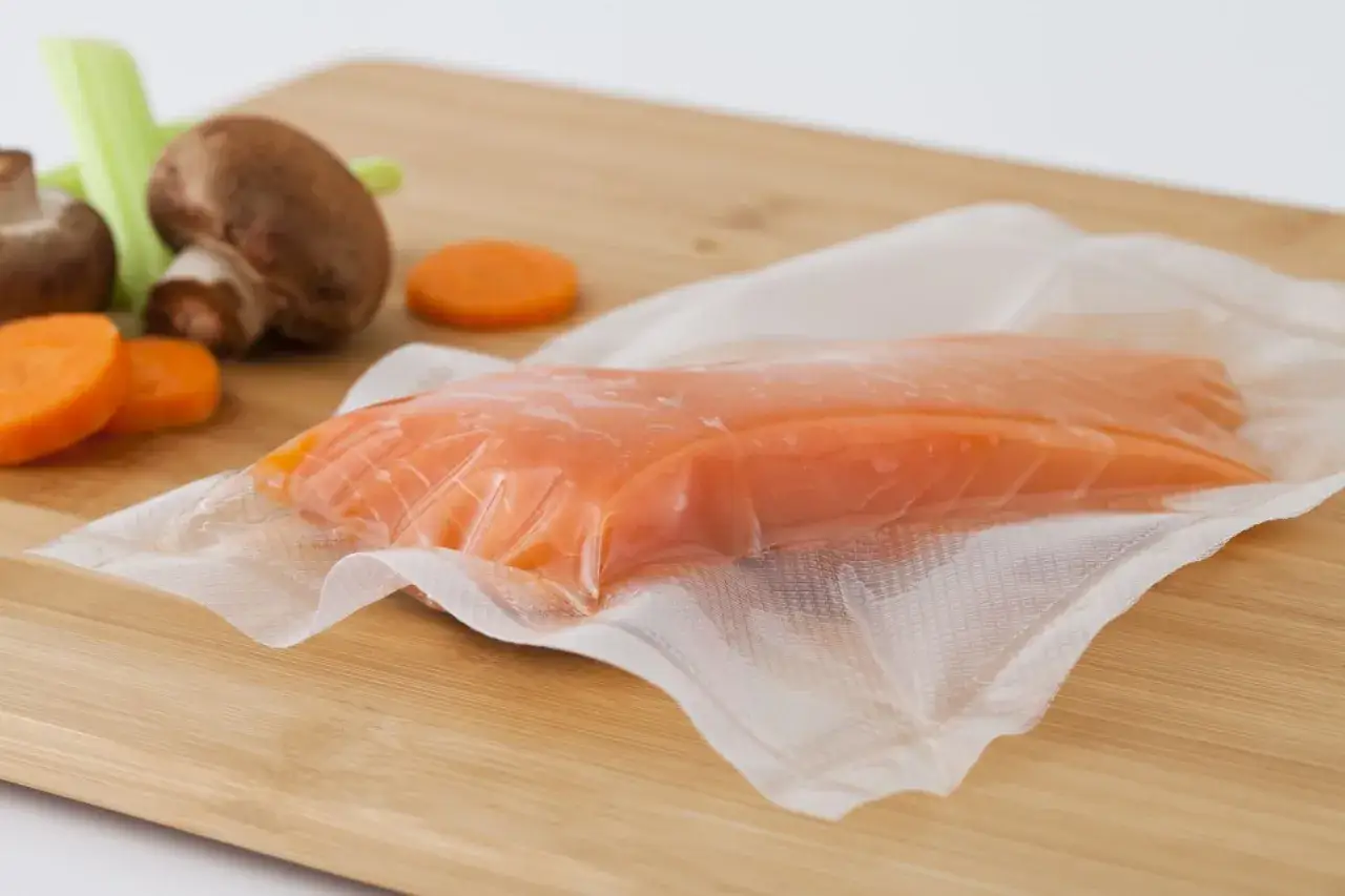 Filete de salmón ahumado envasado al vacío, listo para que se pueda congelar el salmón ahumado. Zanahorias, champiñones y apio al fondo.