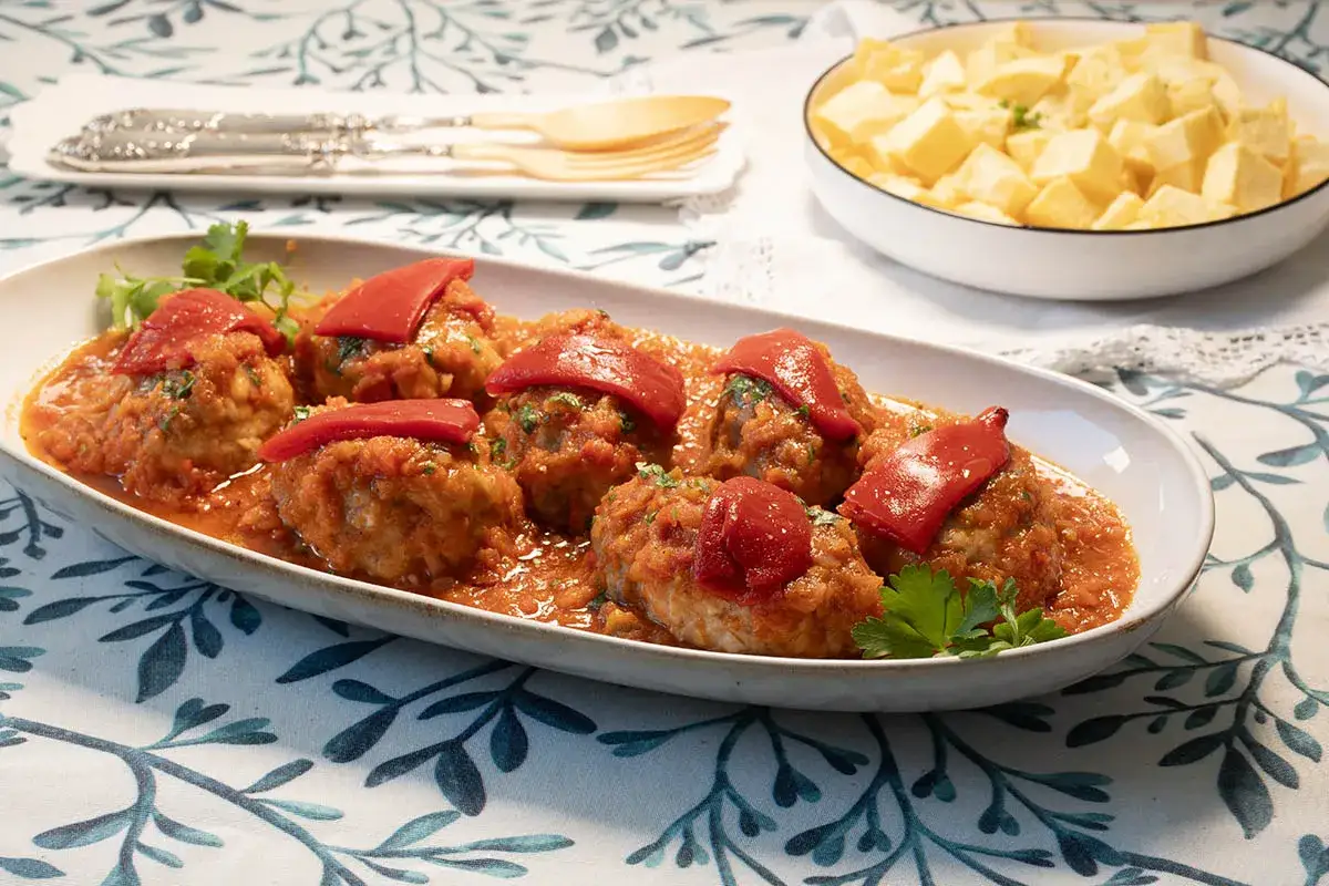 Sabrosos rollos de bonito en salsa de tomate, coronados con pimientos rojos. Acompa&ntilde;ados de patatas fritas en un cuenco.