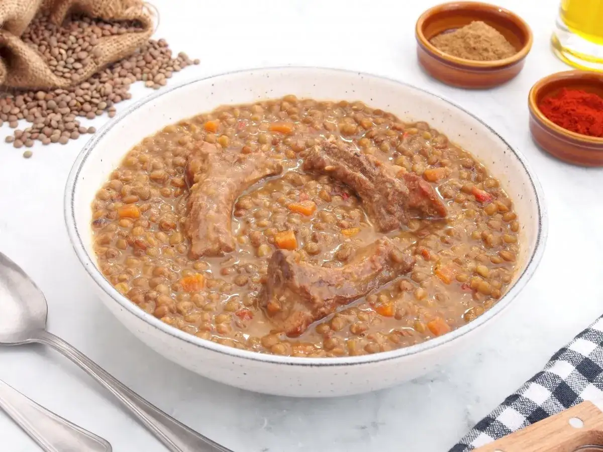 Un reconfortante plato de lentejas con costillas, con trozos de zanahoria y especias al lado.