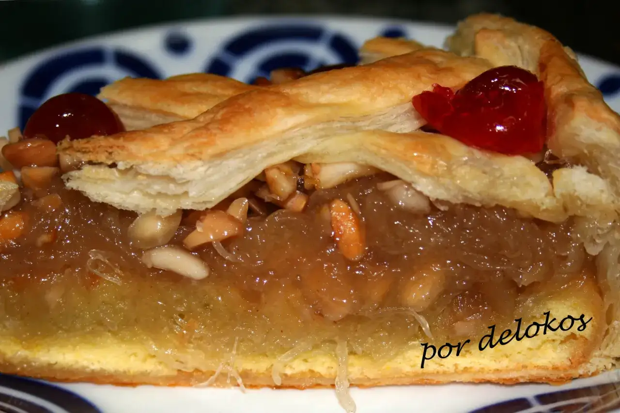 Rebanada de tarta de Mondoñedo con masa hojaldrada, relleno de manzana y almendras, decorada con cerezas rojas.