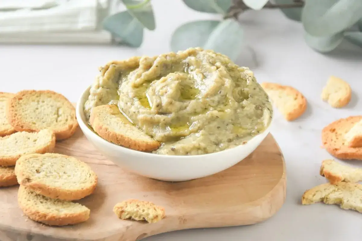Un cremoso pate de berenjena con un chorrito de aceite de oliva, servido con tostaditas crujientes.