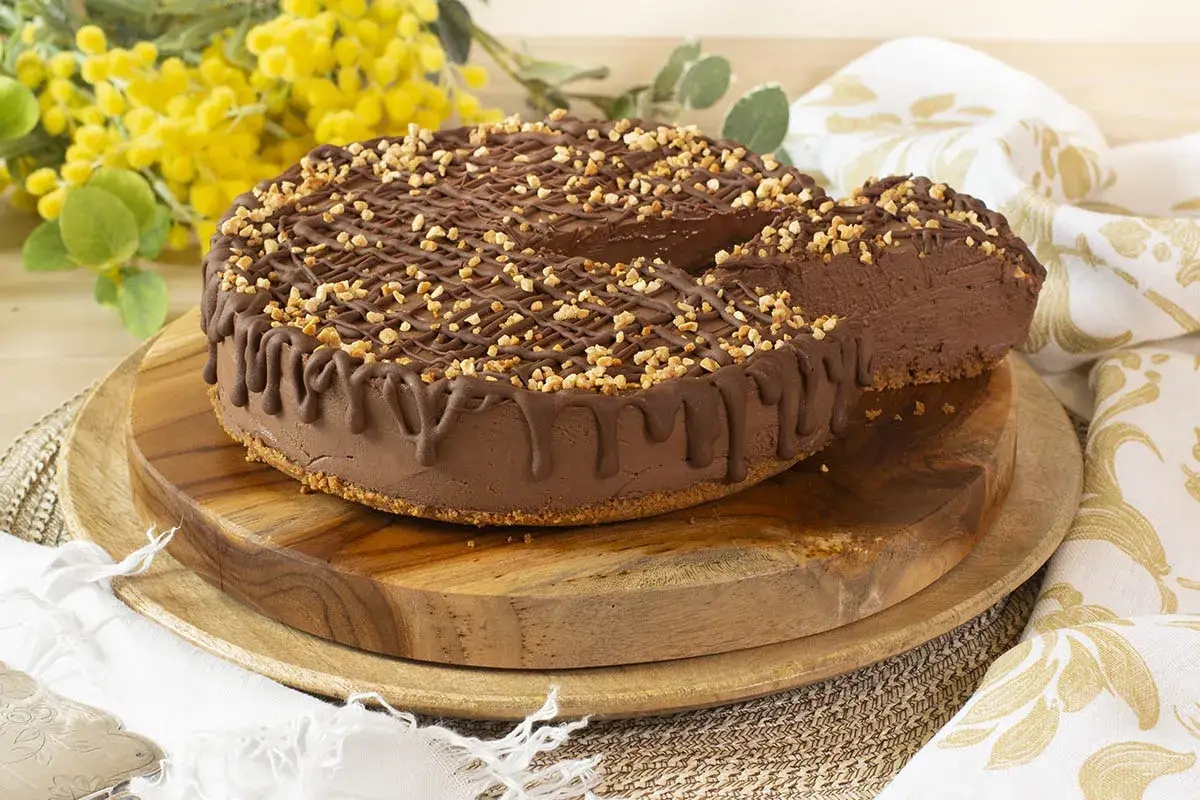 Deliciosa tarta queso mascarpone sin horno, cubierta de chocolate y frutos secos. Una rebanada muestra su interior cremoso.