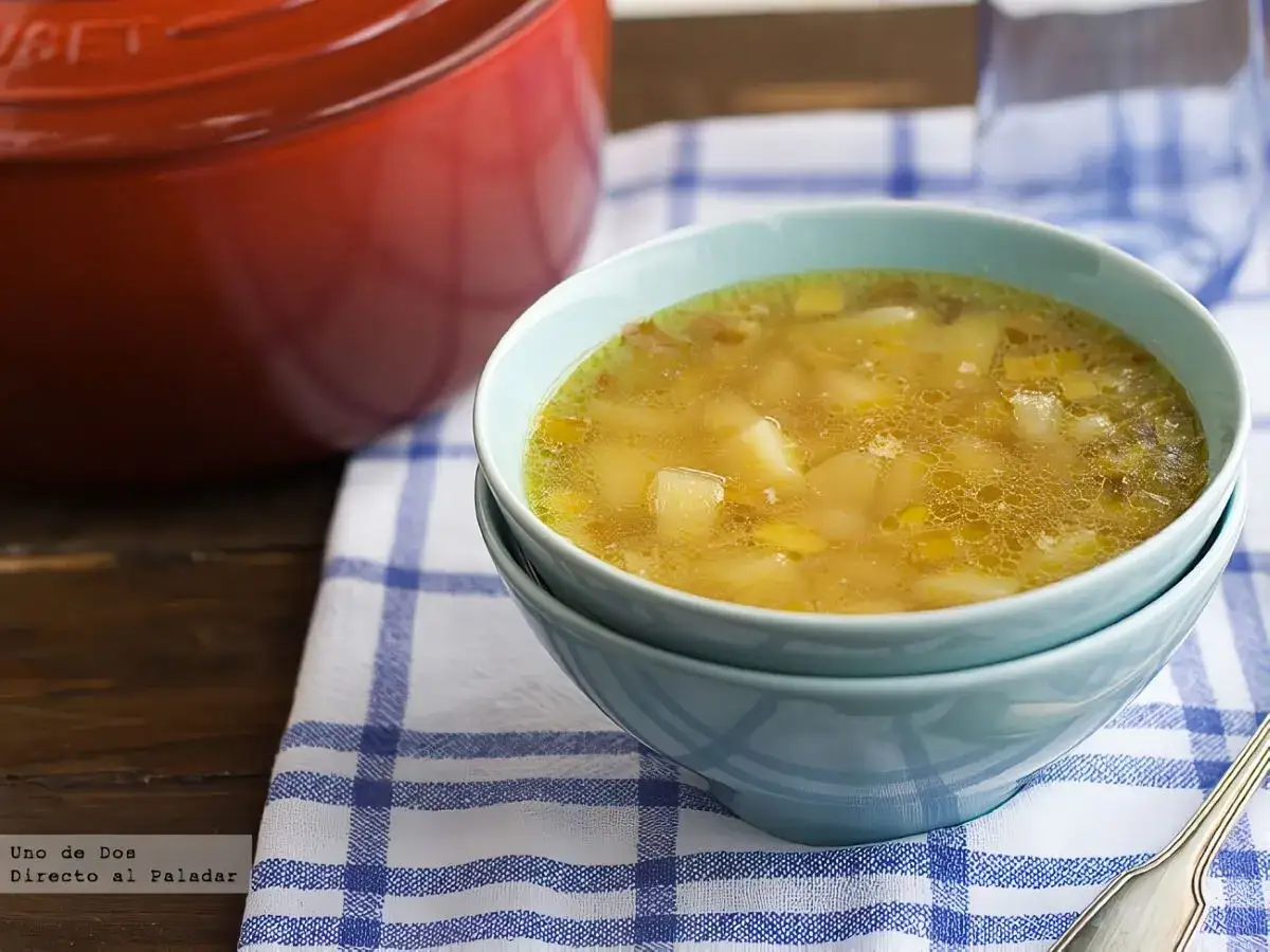 Un reconfortante plato de puerros con patatas en un cuenco azul, junto a una olla roja.