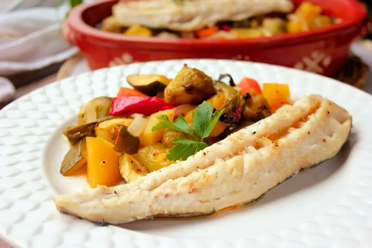 Merluza al horno sin patatas, acompañada de verduras asadas como pimientos, calabacín y cebolla. Un plato saludable y delicioso.