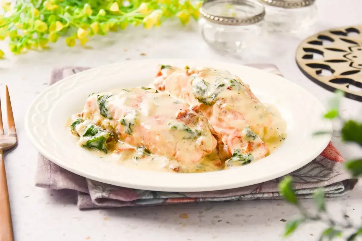 Delicioso salmón a la toscana bañado en una cremosa salsa con espinacas y tomates secos, servido en un plato blanco.