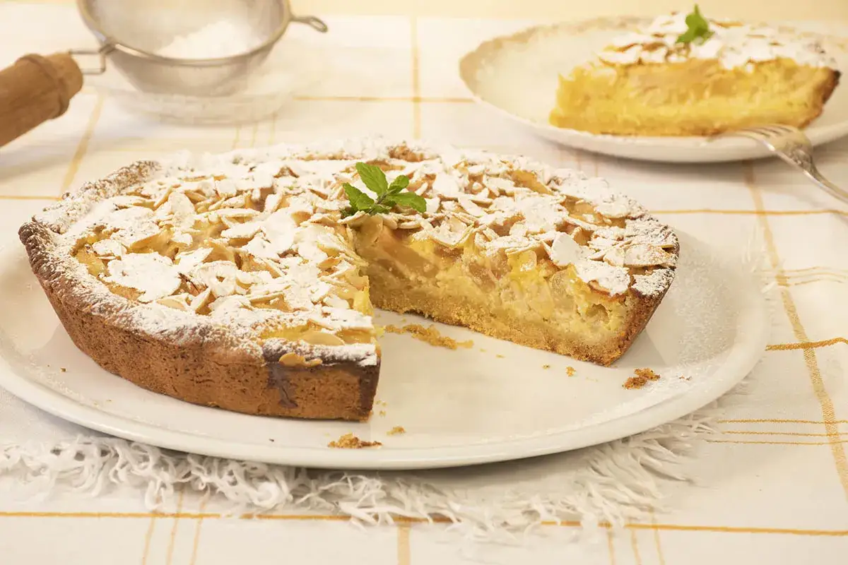 Deliciosa tarta de pera, cubierta de almendras laminadas y espolvoreada con az&uacute;car glas. Una rebanada ya servida.
