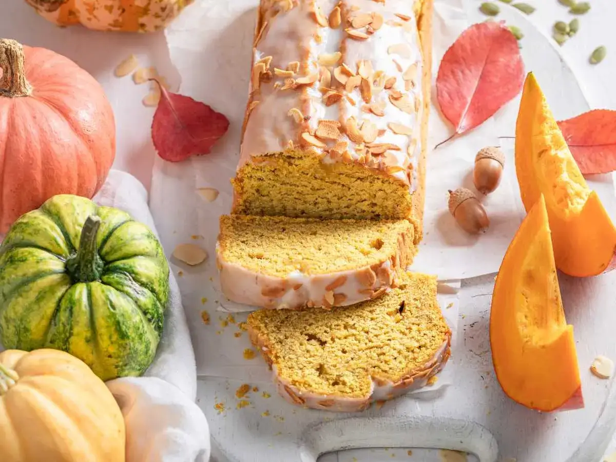 Delicioso bizcocho de calabaza Thermomix, glaseado y decorado con almendras. Rodeado de calabazas y hojas de otoño.