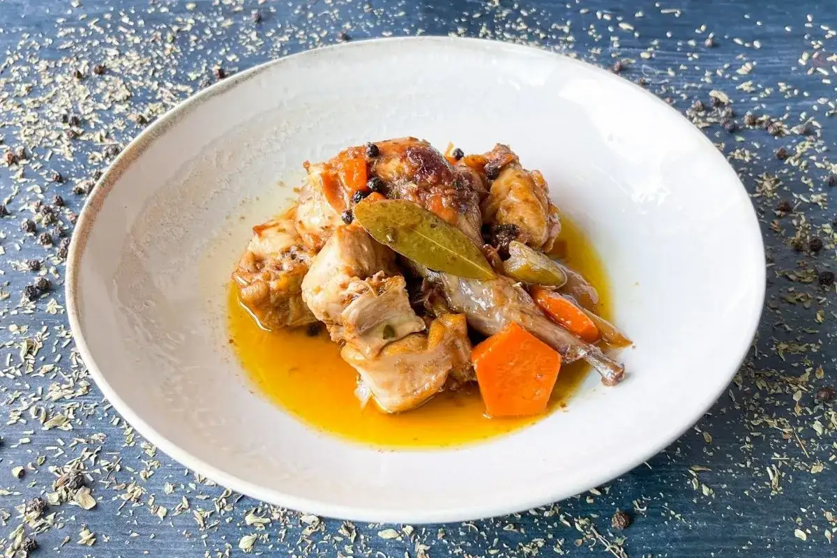 Sabroso conejo en escabeche, con zanahoria y laurel, servido en un plato blanco.