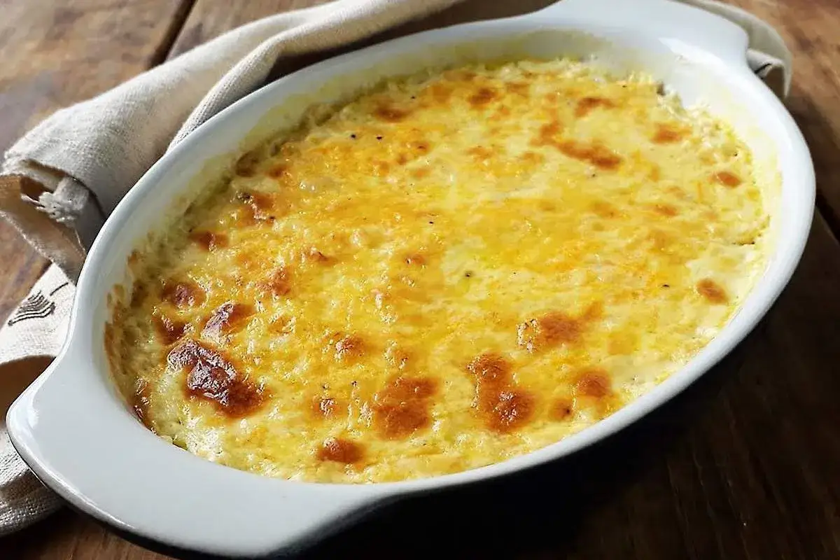 Bacalao a la nata gratinado, burbujeante y dorado en una fuente ovalada blanca, listo para servir.