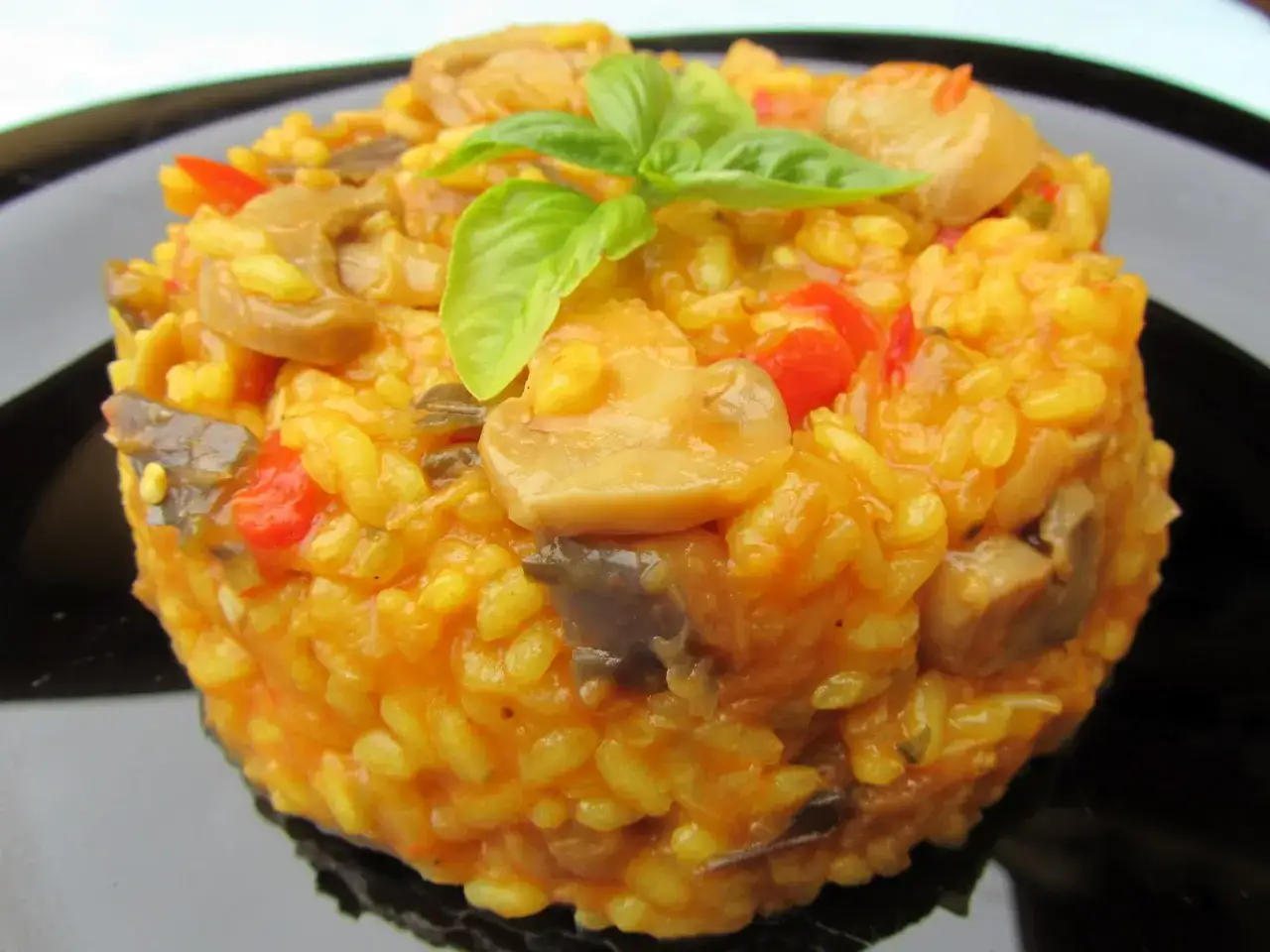 Arroz con verduras y champiñones, preparado en Thermomix, servido en un plato negro y decorado con hojas de albahaca fresca.