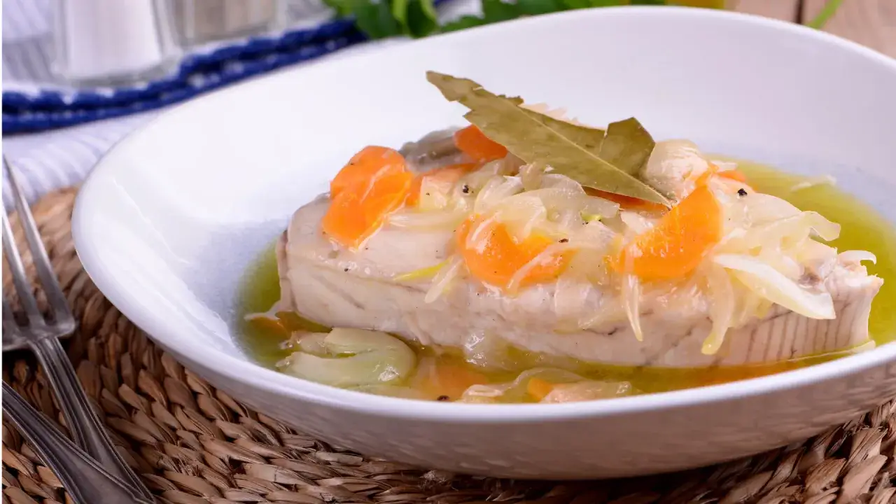 Delicioso at&uacute;n en escabeche con zanahoria y cebolla, servido en un plato blanco sobre una base de mimbre.
