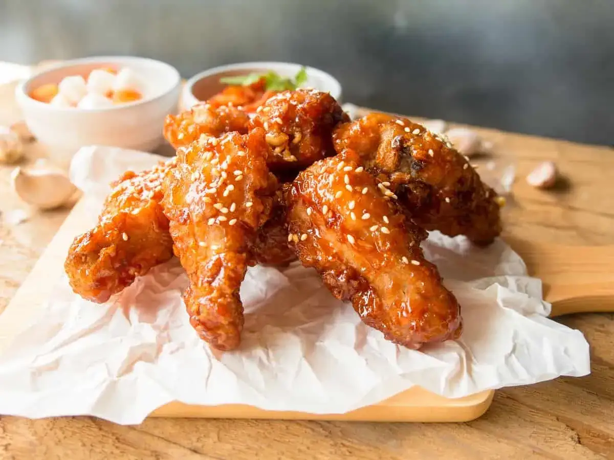 Deliciosas alitas de pollo frito coreano glaseadas y espolvoreadas con semillas de s&eacute;samo, servidas sobre papel encerado.