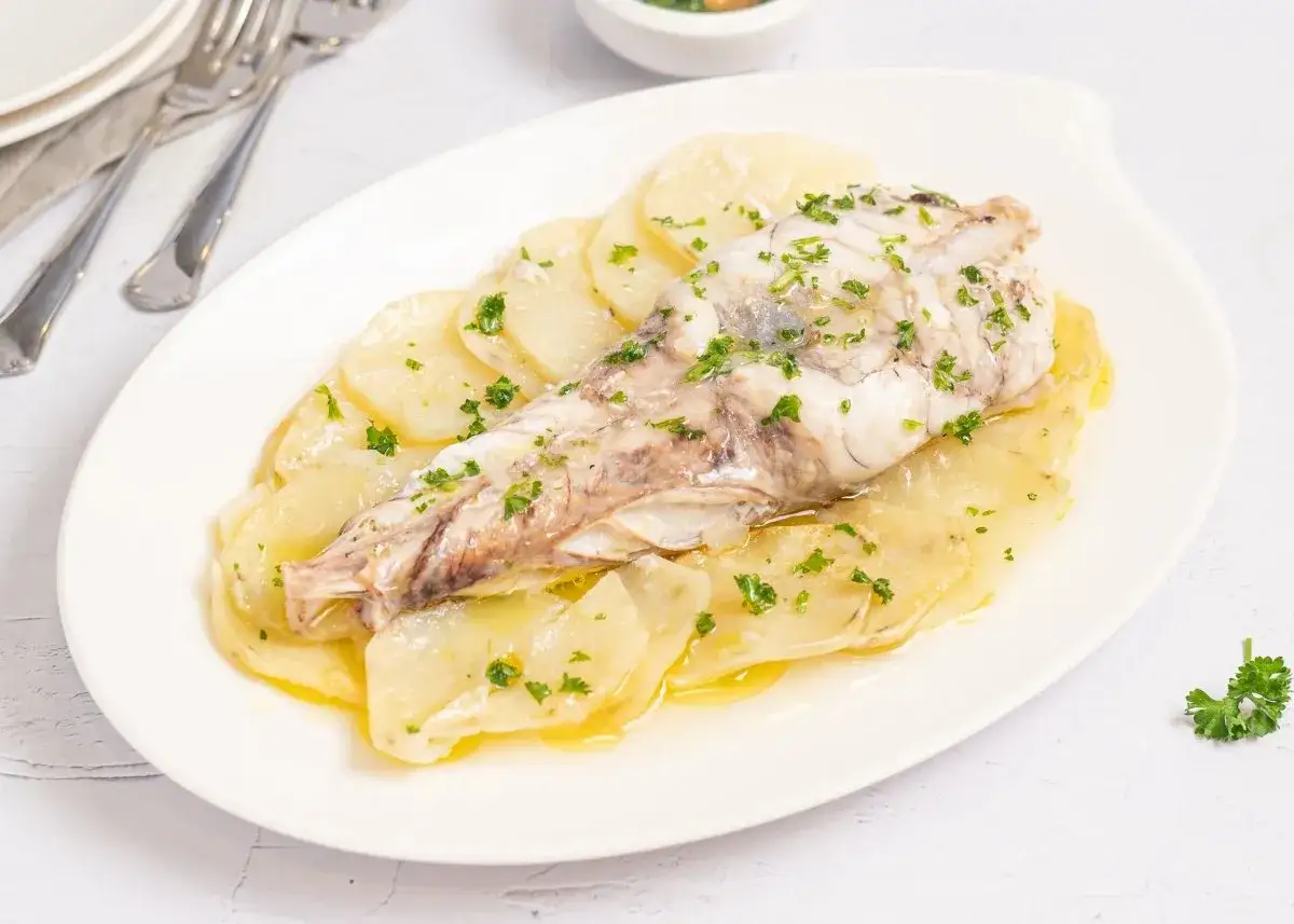 Delicioso rape al horno sobre una cama de patatas laminadas, todo espolvoreado con perejil fresco.