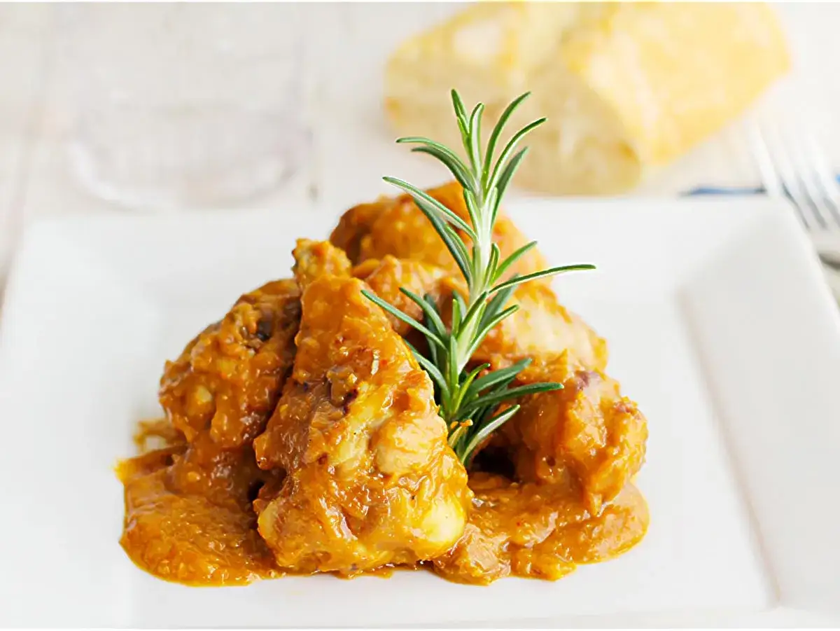 Sabroso pollo con almendras en una salsa dorada, adornado con romero fresco.