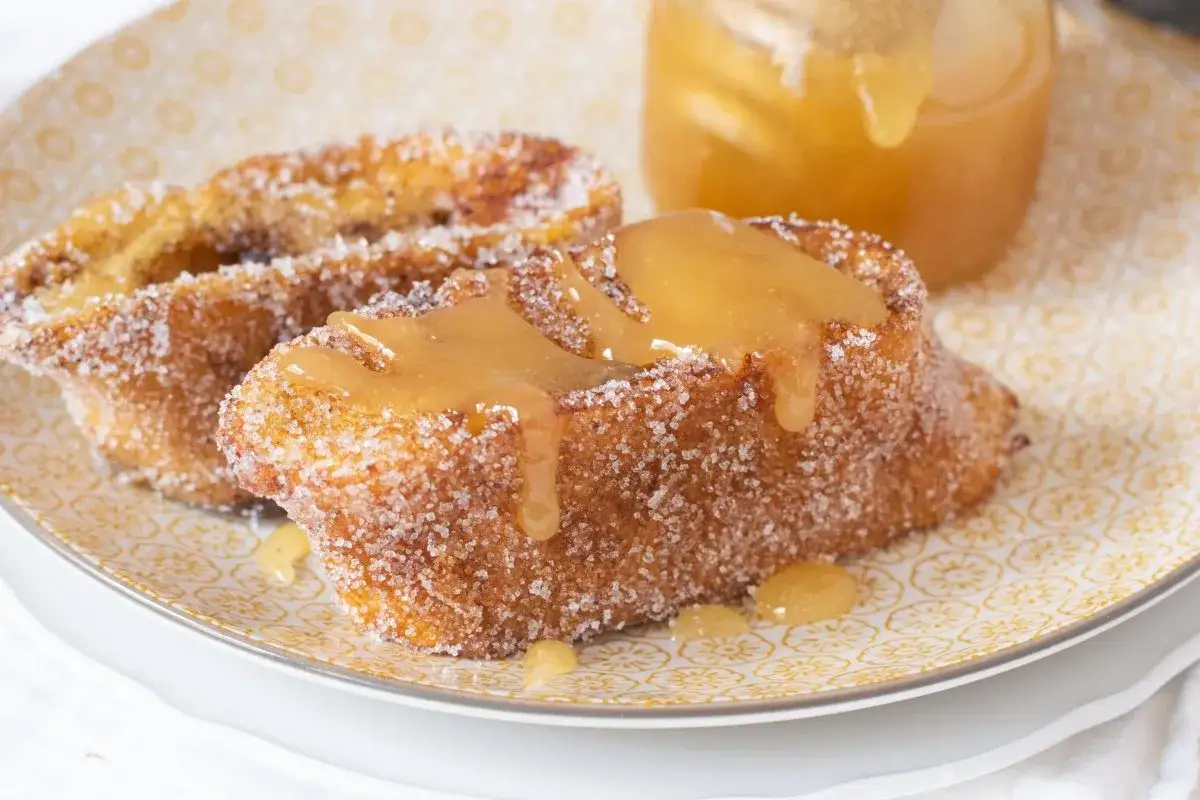 Torrijas de miel, doradas y rebozadas en az&uacute;car, con un jarabe dorado cayendo.