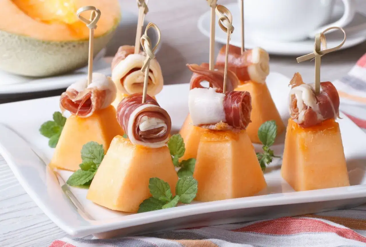 Delicioso melon con jamon, cortado en cubos y enrollado con jamon serrano, adornado con hojas de menta.