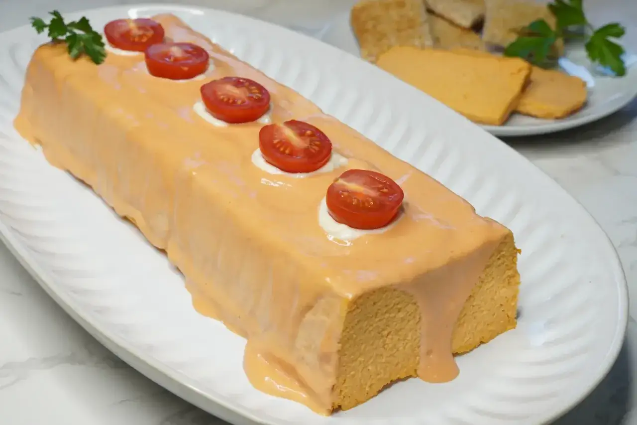 Pastel de cabracho cubierto con salsa rosada, decorado con tomates cherry y perejil. Servido en plato blanco.