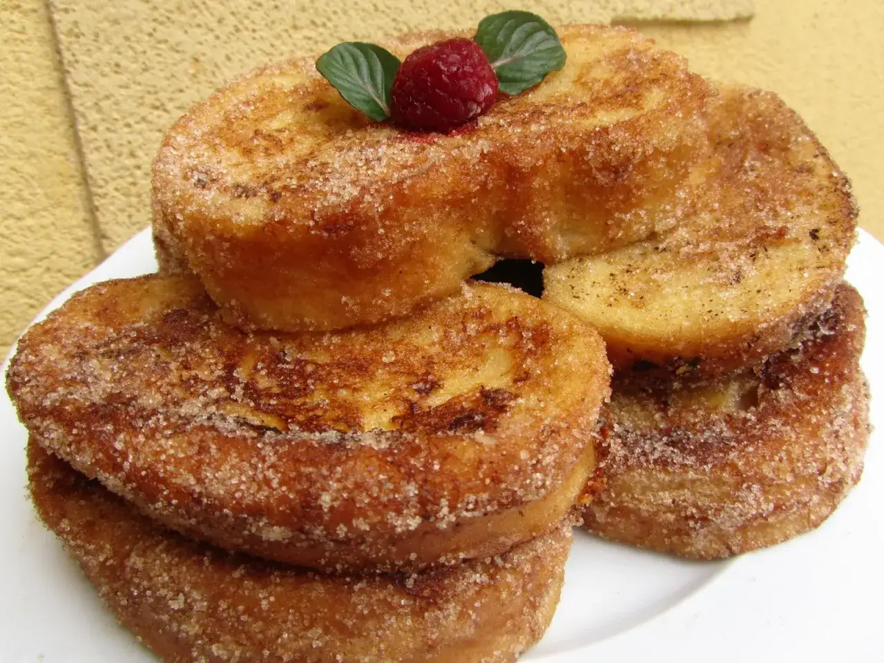 Torrijas doradas y crujientes, espolvoreadas con az&uacute;car y canela, perfectas para hacer en Thermomix. Decoradas con una frambuesa y hojas verdes.