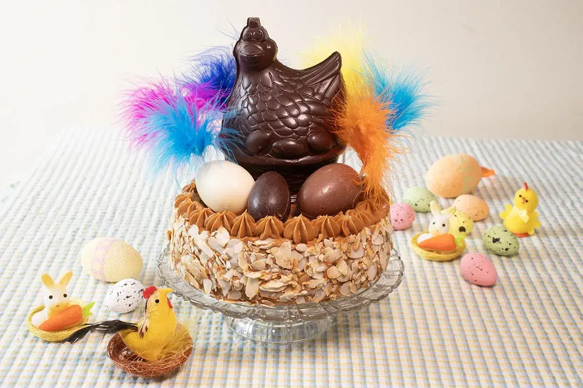 Tarta decorada con un pollo de chocolate, huevos y plumas, ideal para una receta de monas de Pascua.