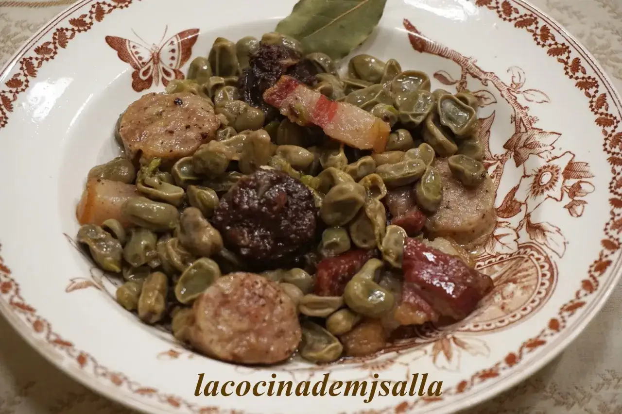 Plato de habas a la catalana con trozos de panceta y morcilla, servido en una vajilla con decoraciones de mariposas y flores.