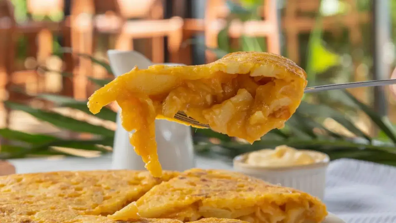 Un tenedor levanta un trozo jugoso de tortilla de patatas, mostrando su interior tierno y dorado.