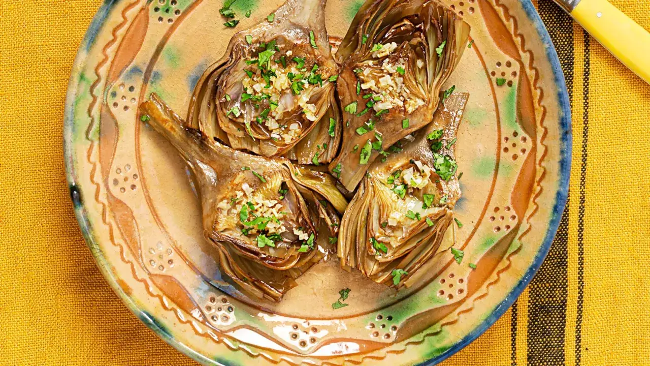 Alcachofas hervidas, cortadas y rellenas de ajo y perejil, servidas en un plato rústico. Ideales para recetas con alcachofas hervidas.