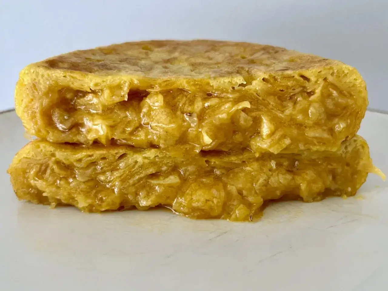 Dos porciones de tortilla con patatas de bolsa, doradas y jugosas, apiladas sobre un plato blanco.