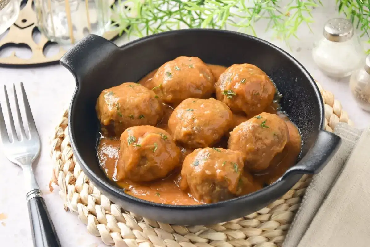 Deliciosas polpette al sugo, jugosas albóndigas en salsa de tomate, servidas en una cazuela negra sobre una esterilla de mimbre.