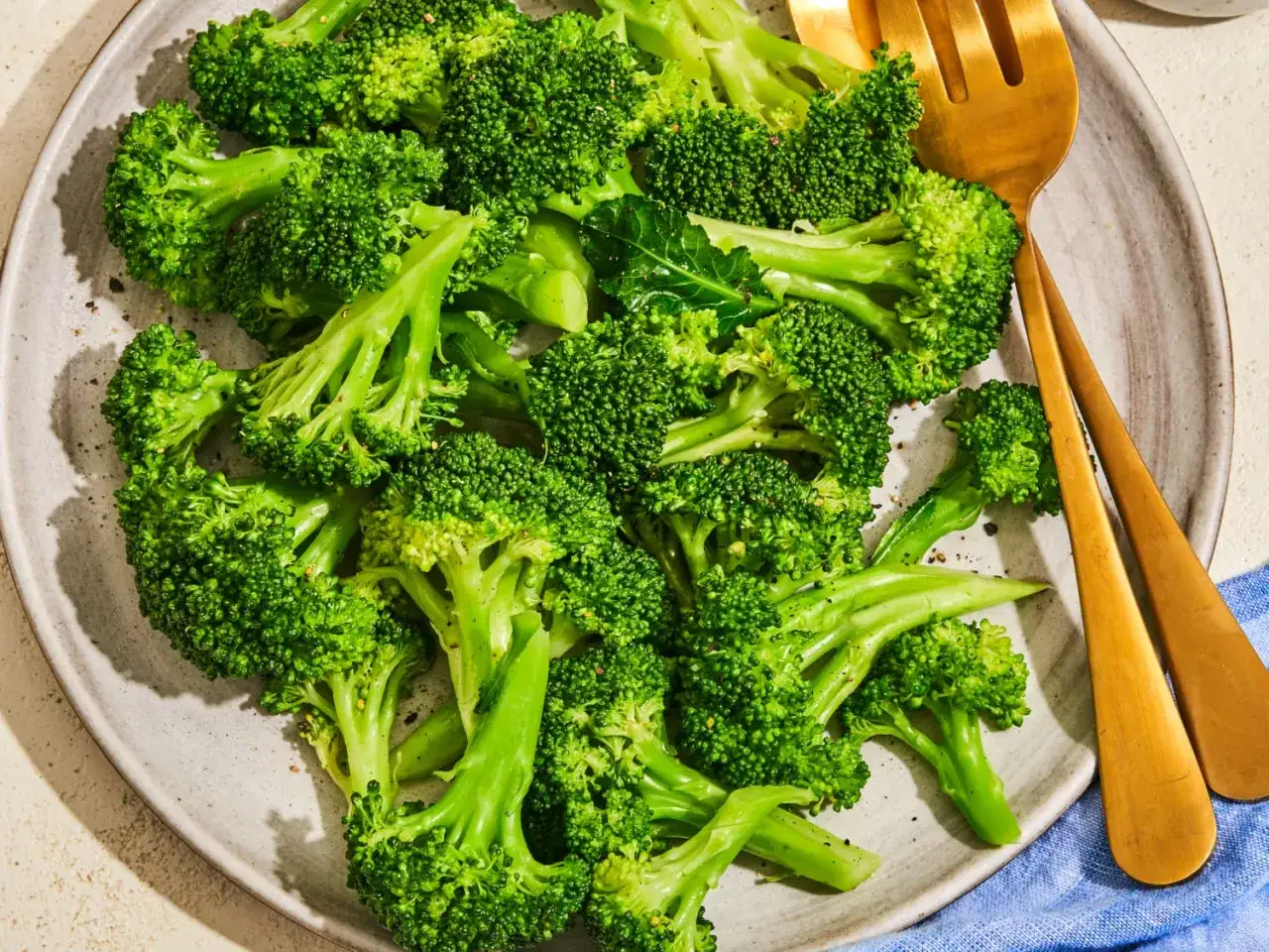 Un plato de brócoli al vapor, vibrante y verde, con tenedores dorados listos para disfrutar de esta saludable opción.