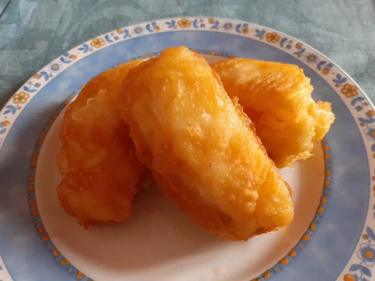 Tres trozos de bacalao rebozado crujiente dorados y apetitosos en un plato azul y blanco.