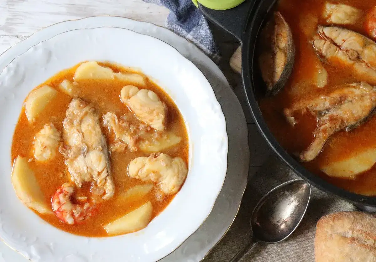 Un delicioso suquet de pescado con patatas y gambas, servido en un plato blanco y una cazuela.