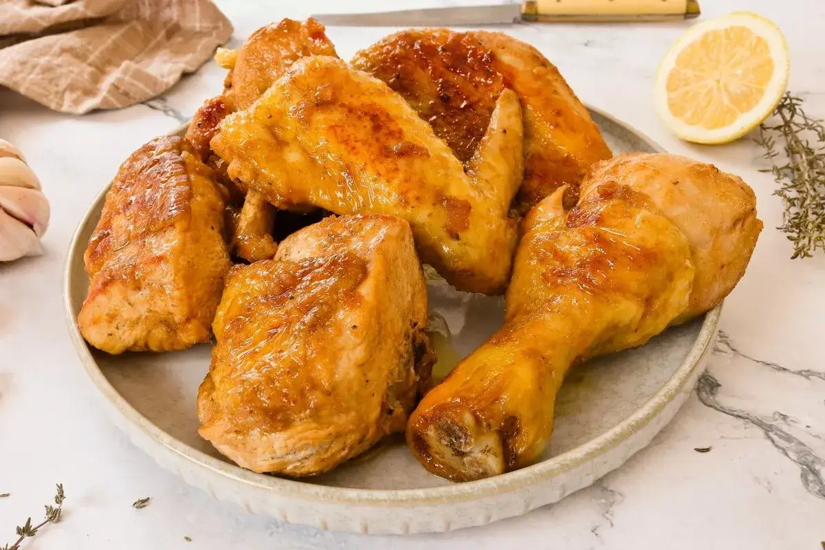 Plato de pollo al horno jugoso y dorado, con trozos de pechuga, muslos y alitas. Acompañado de limón y hierbas.