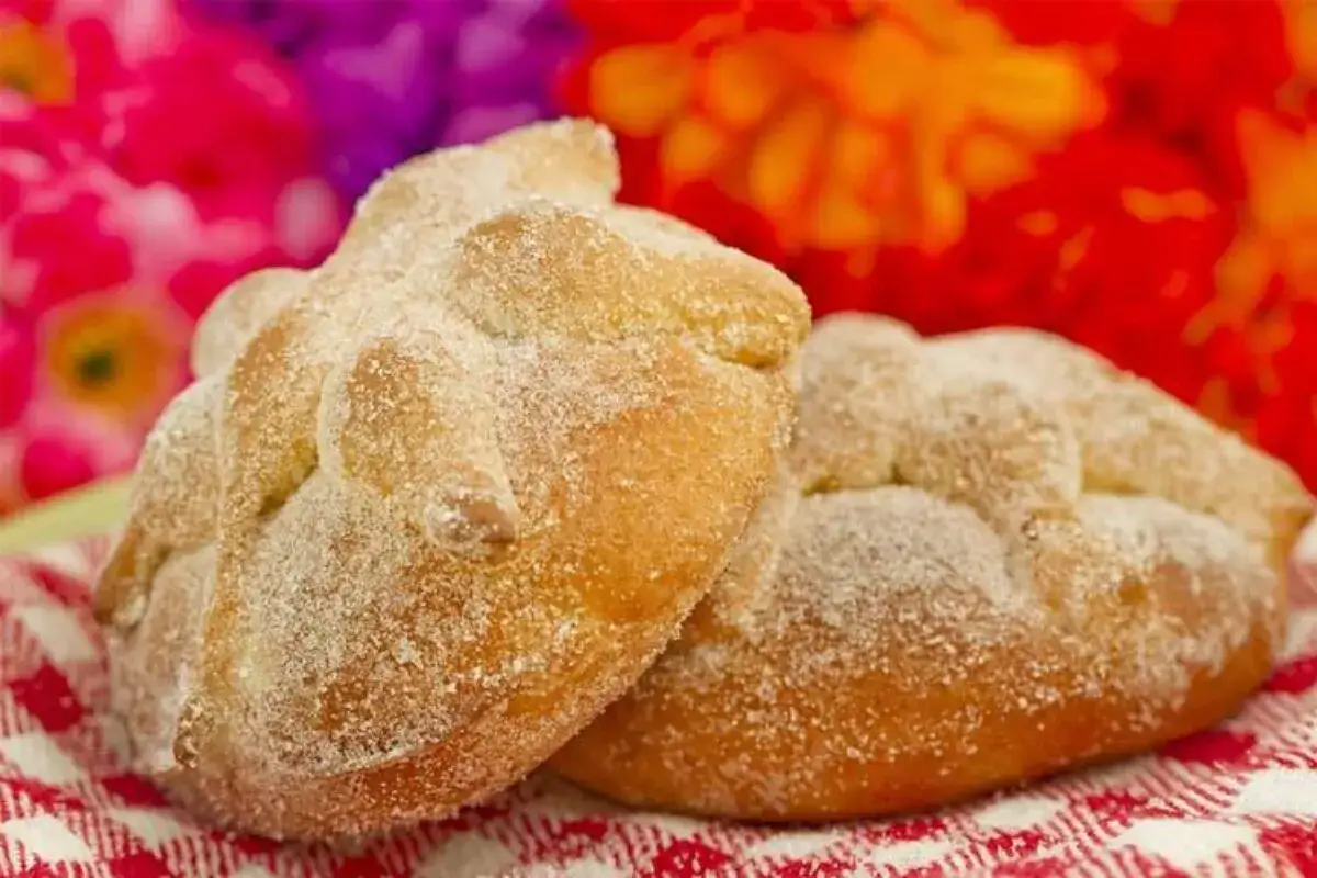 Dos panes de muerto cubiertos de azúcar, con flores de cempasúchil y terciopelo al fondo.